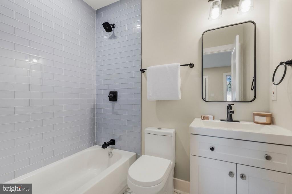 Bathroom with a subway-tile tub surround, black fixtures, toilet, and white vanity.
