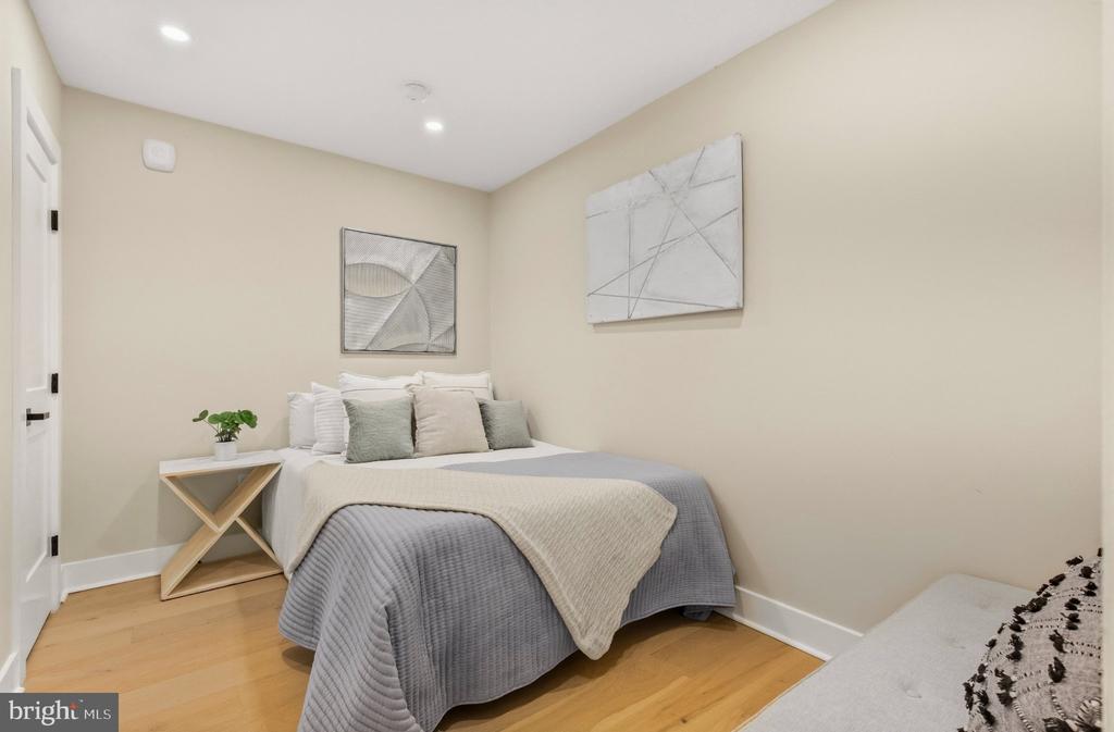 Staged bedroom with gray and cream bedding, light hardwood floors, and abstract wall art.