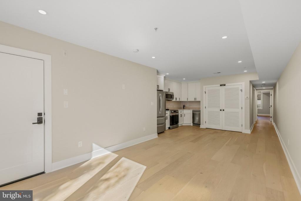 Unfurnished open-plan living area with a compact white kitchen, stainless steel appliances, and light hardwood floors.