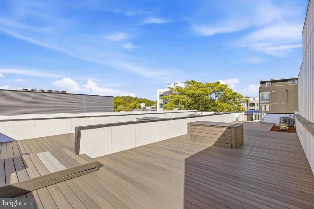 Rooftop deck with built-in bench seating, a raised planter, and neighboring buildings beyond.