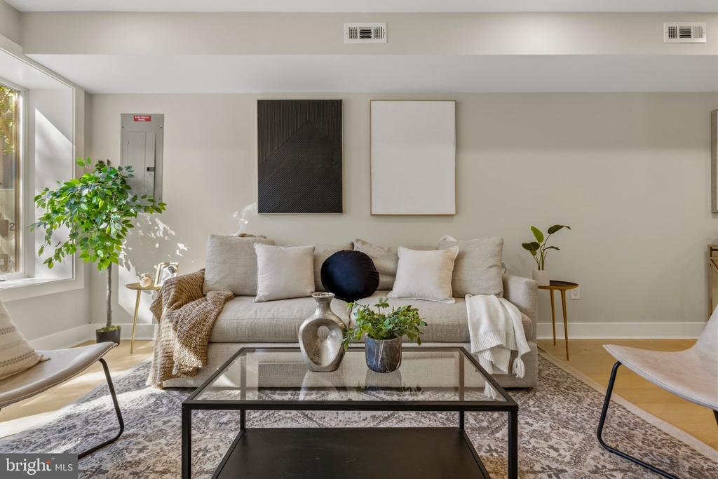 Staged living room with a gray sofa, glass coffee table, and large sunlit window.