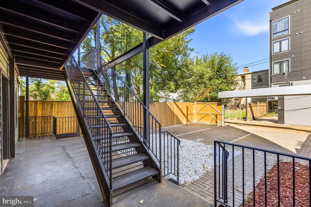 Apartment courtyard with black metal stairs, covered walkway, and wooden fence.