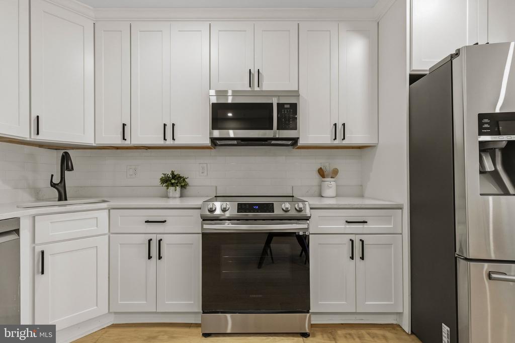 White kitchen with shaker cabinets, stainless steel appliances, subway tile backsplash, and light wood flooring.