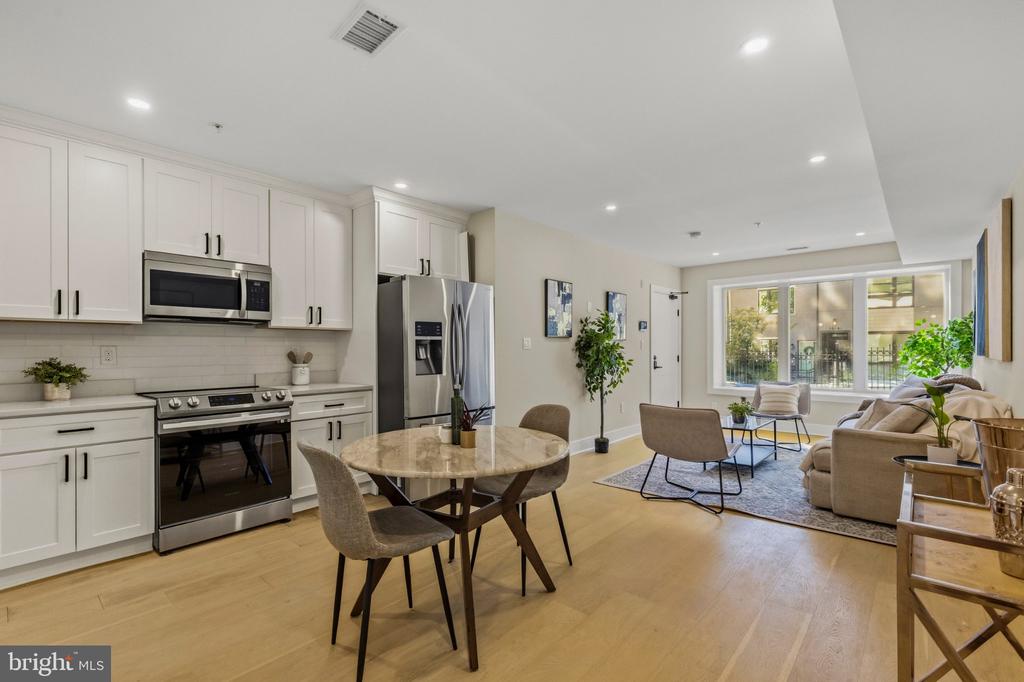 Open-plan kitchen and living room with white cabinets, stainless appliances, and large windows overlooking greenery.