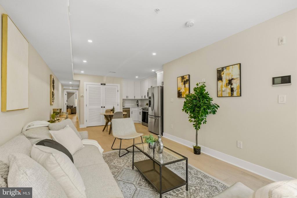 Open-plan living room with a light sofa and glass coffee table, dining area, and white kitchen.