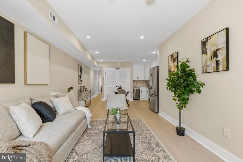 Staged living room with a cream sofa, glass coffee table, and open kitchen beyond.
