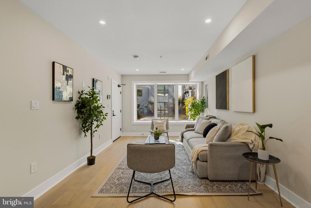 Staged living room with a gray sofa, patterned rug, and large windows.
