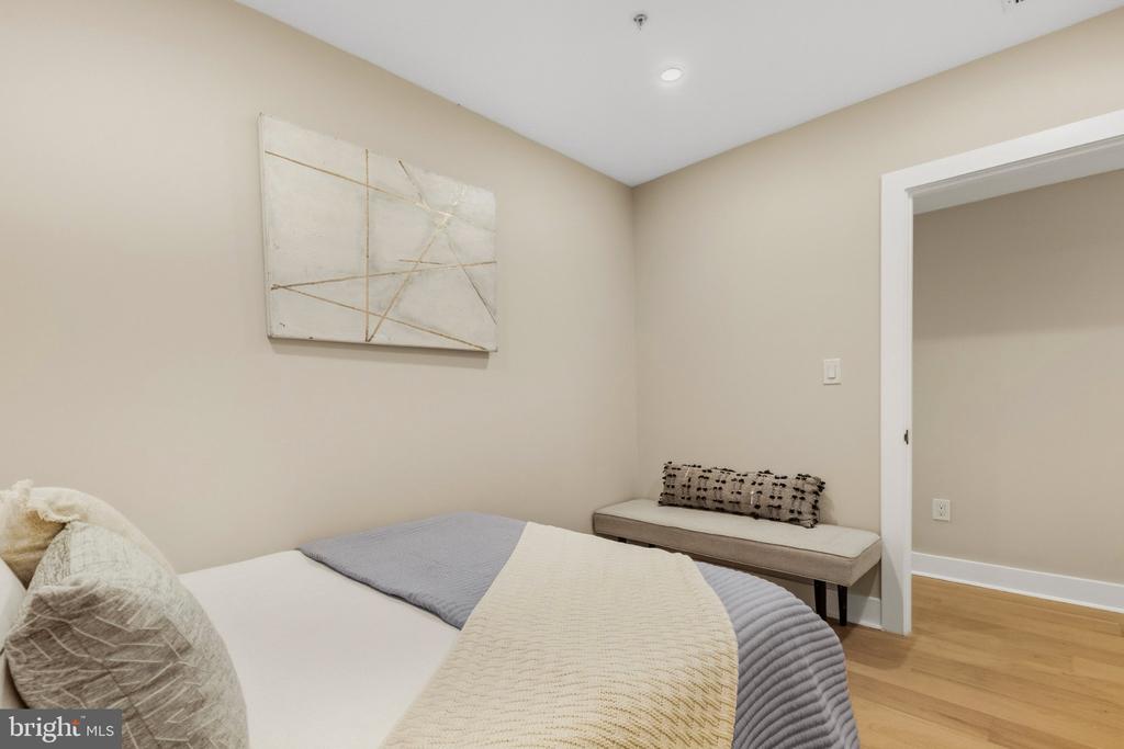 Bedroom with white and gray bedding, an upholstered bench, and abstract wall art.
