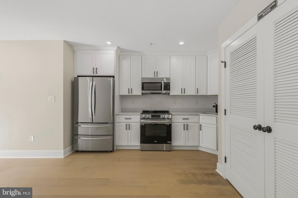 Kitchen with white cabinets, stainless-steel appliances, and light wood flooring.