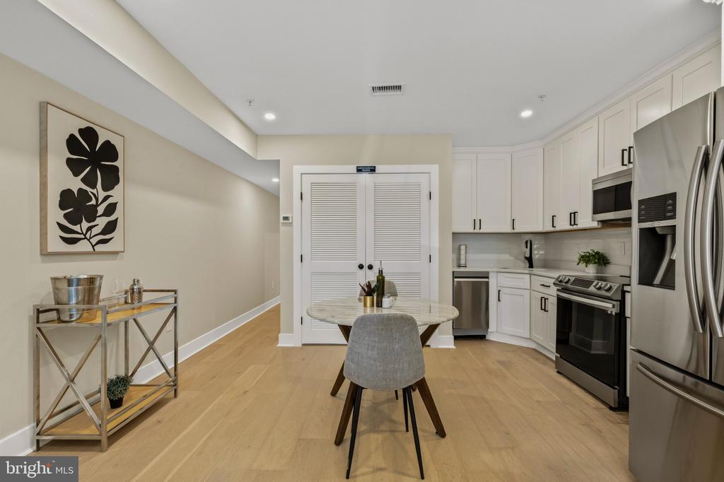 Kitchen with white cabinets, stainless steel appliances, and a small dining table on light wood floors.