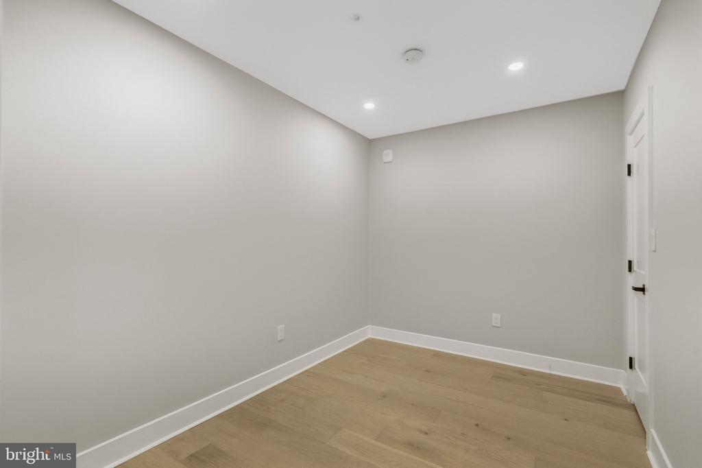 Empty room with pale wood floors, gray walls, recessed lights, and a white door.