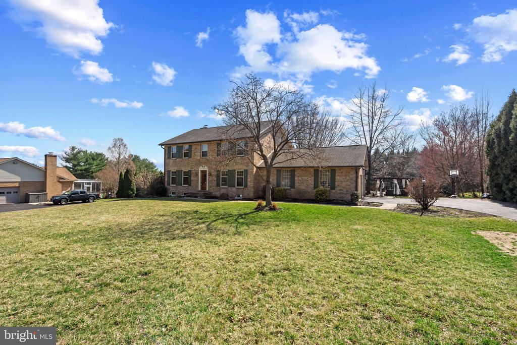 Two-story brick house behind a broad lawn, with a driveway and basketball hoop.