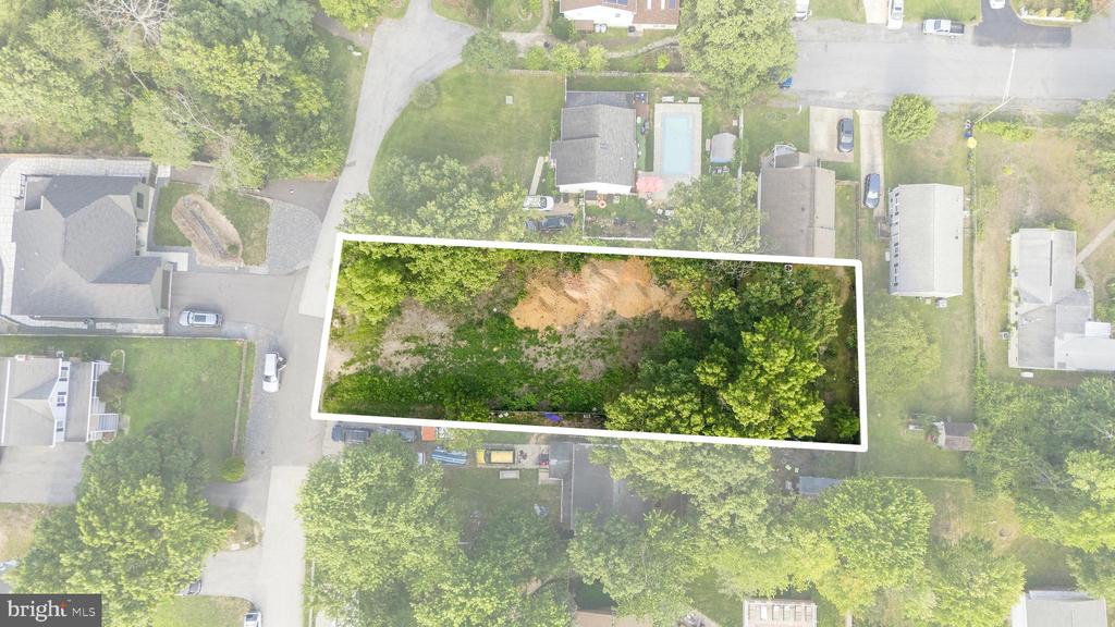 Aerial view of a wooded vacant lot outlined in white among neighboring homes.