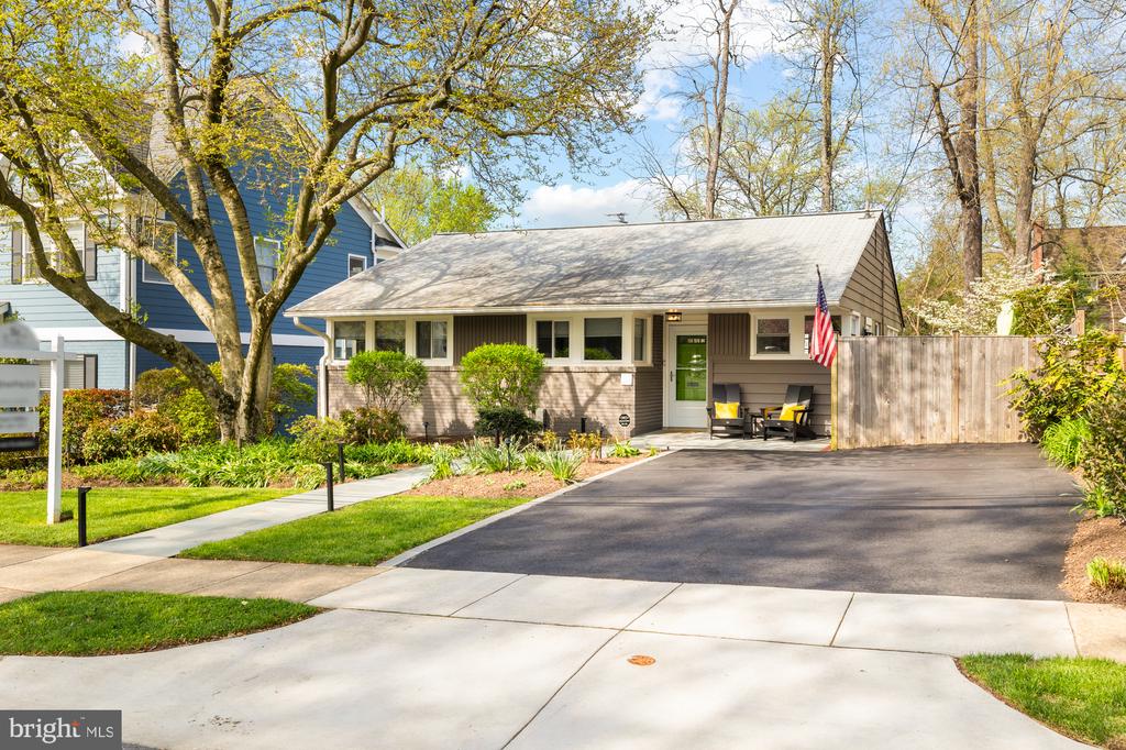 Single-story gray home with a green front door, covered patio, American flag, and wide paved driveway.