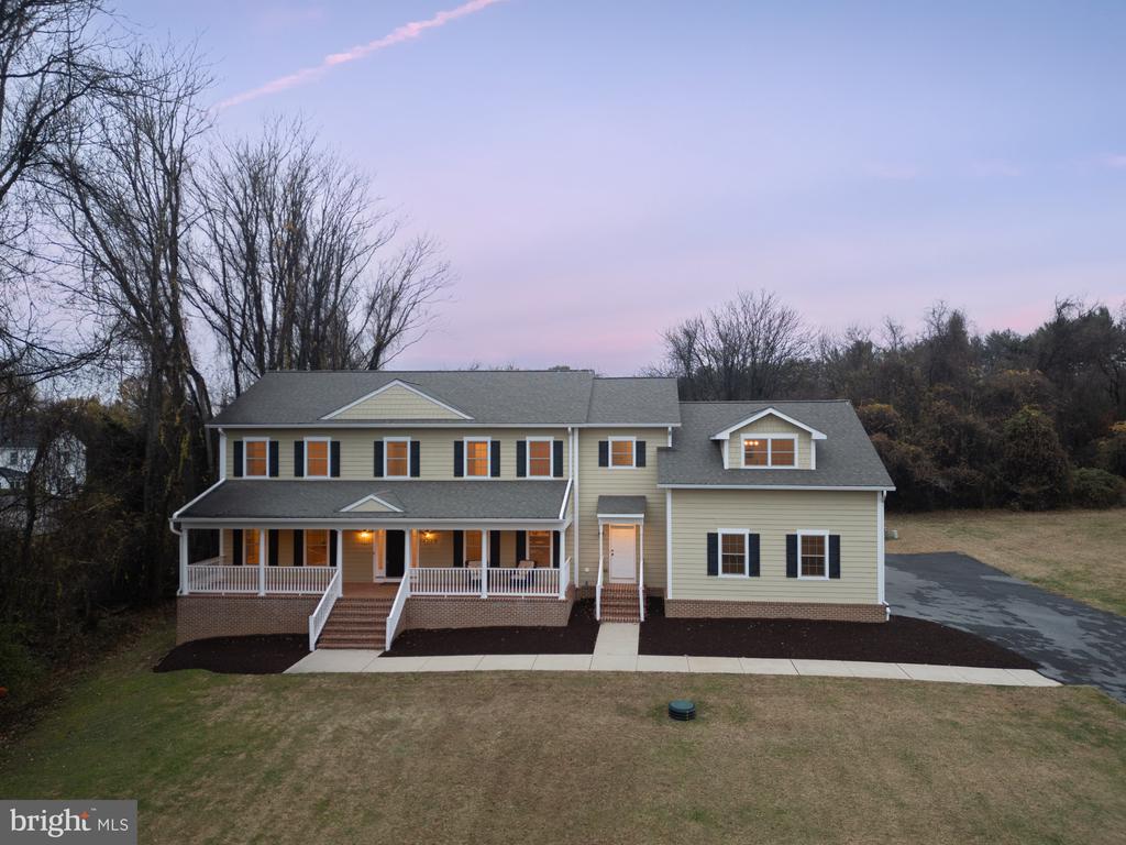 Two-story beige house with a covered porch and glowing windows at dusk.
