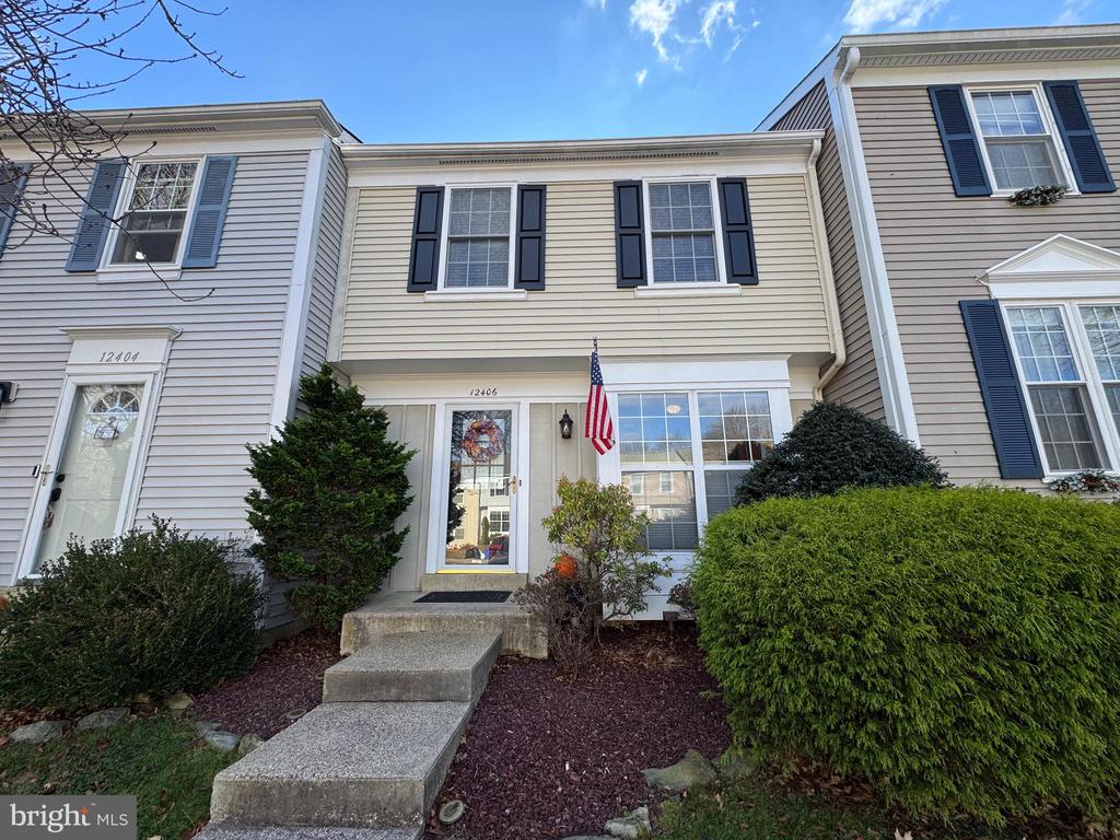 Attached home with beige siding, dark shutters, an American flag, and a walkway to the front door.