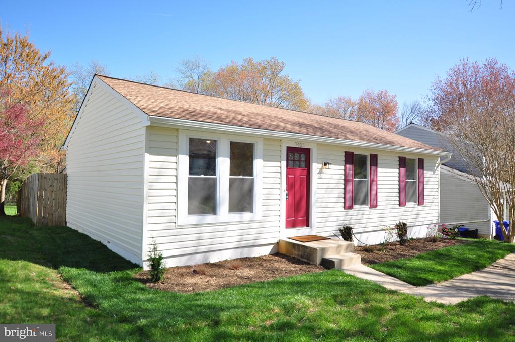 Single-story white house with a red front door and shutters, lawn, and autumn trees.