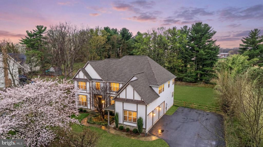 Aerial view of a white two-story home with gabled roofs, a broad lawn, and a flowering tree.