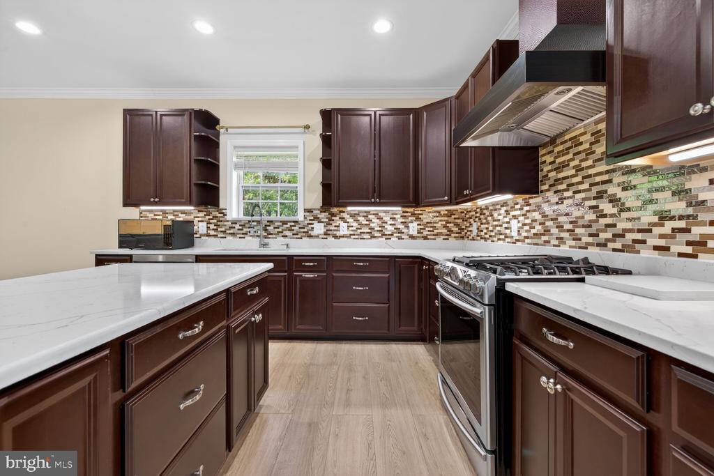 Kitchen with dark wood cabinets, white counters, mosaic backsplash, and a stainless steel range.