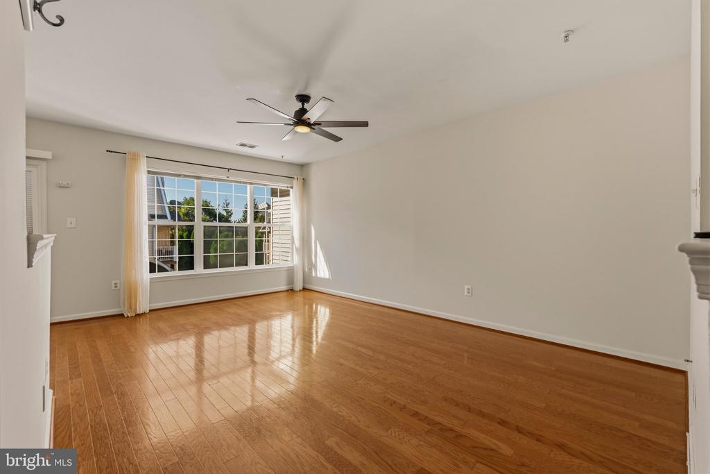 Empty living room with hardwood floors, a large curtained window, and a ceiling fan.