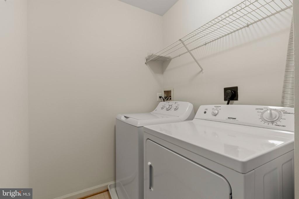 Laundry room with a white washer and dryer beneath a high wire shelf.