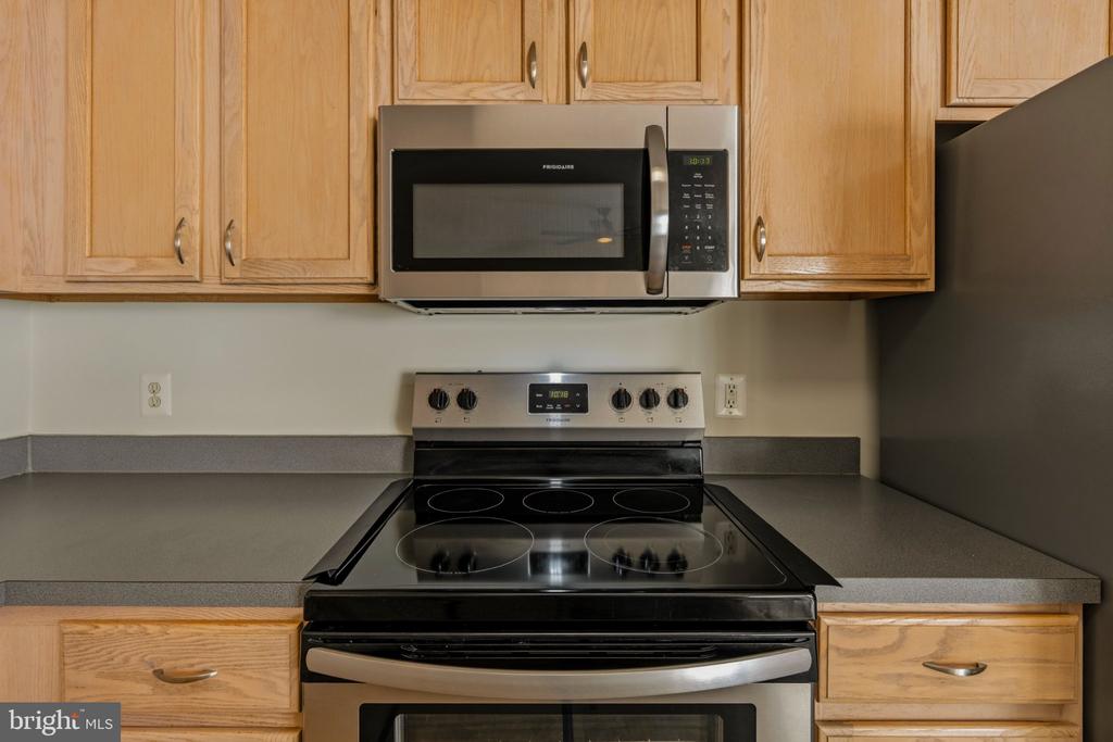 Kitchen with light wood cabinets, gray countertops, and a black electric range beneath a stainless steel microwave.