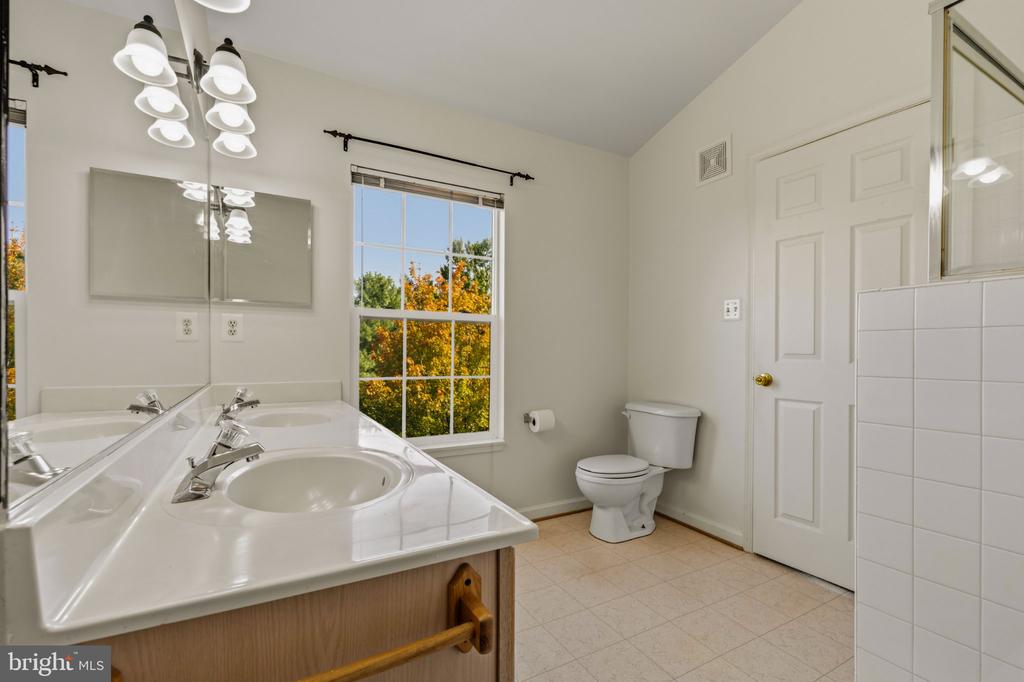 Bathroom with a double-sink vanity, large mirror, and window overlooking autumn trees.