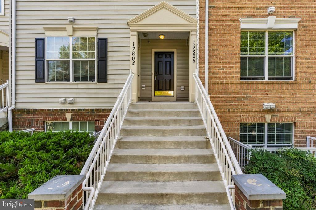 Condominium entrance with broad concrete stairs, white railings, and neighboring numbered doors.