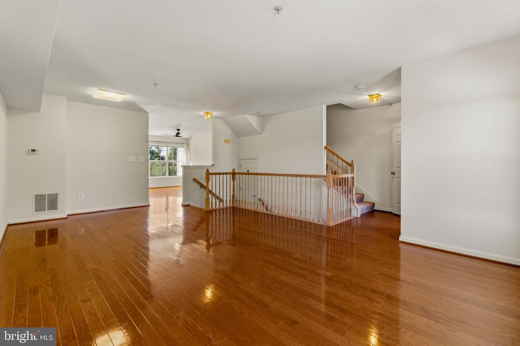 Open interior with glossy hardwood floors, a central stair railing, and a bright window.