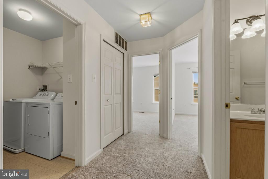 Carpeted hallway with a washer and dryer in the laundry area and a bathroom vanity nearby.