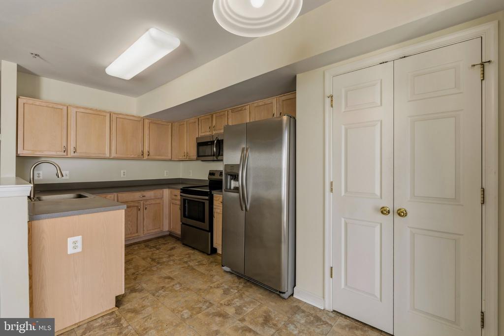 Kitchen with light wood cabinets, stainless steel appliances, and a sink peninsula beside white double doors.
