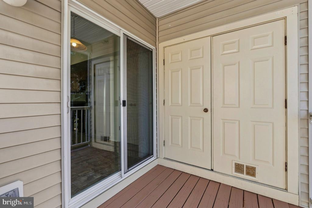 Small deck with brown plank flooring, beige siding, sliding glass door, and white double entry door.