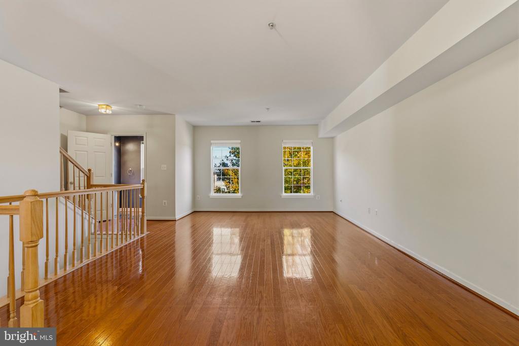 Vacant living area with polished hardwood floors, two windows, and a staircase with wood railing.