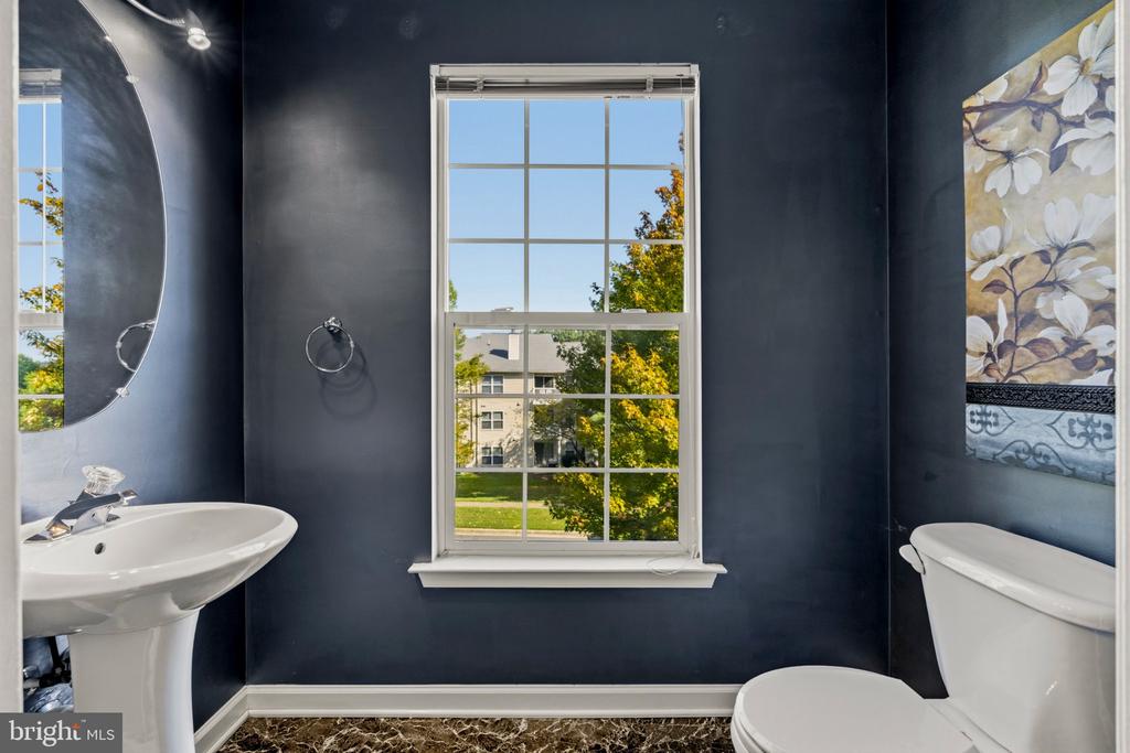 Bathroom with navy walls, a white pedestal sink and toilet, and a large window overlooking trees.