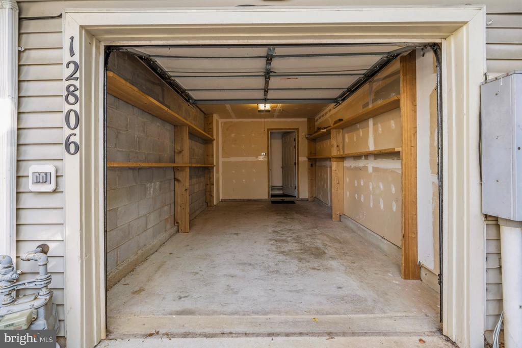 Vacant garage with concrete floor, wooden storage shelves, and an interior door at the back.