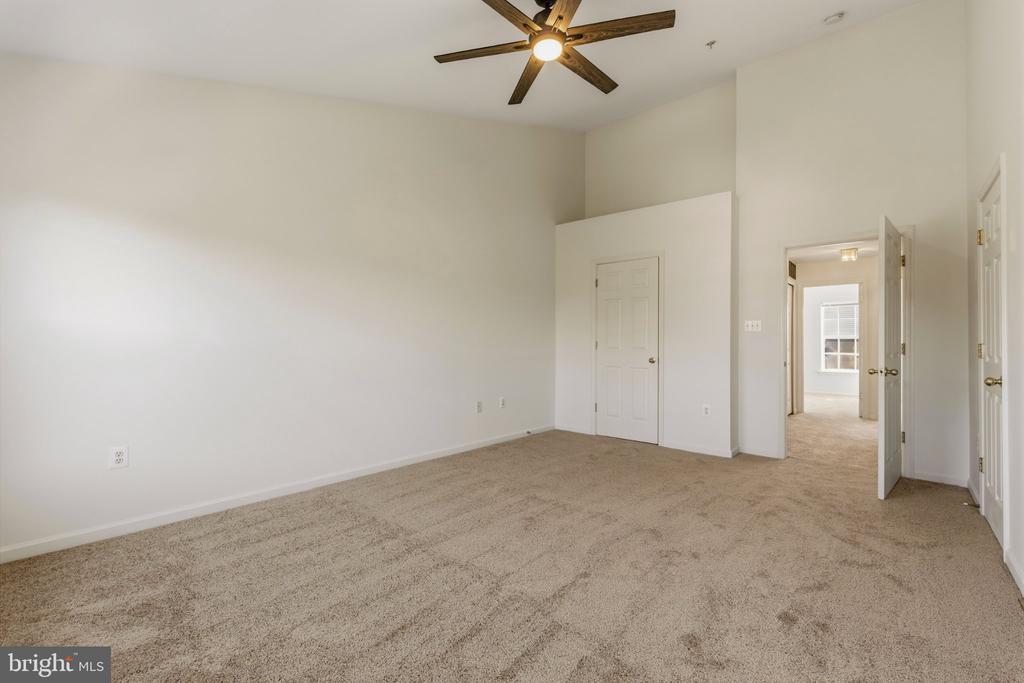 Empty carpeted bedroom with a ceiling fan and open doorways to adjoining rooms.
