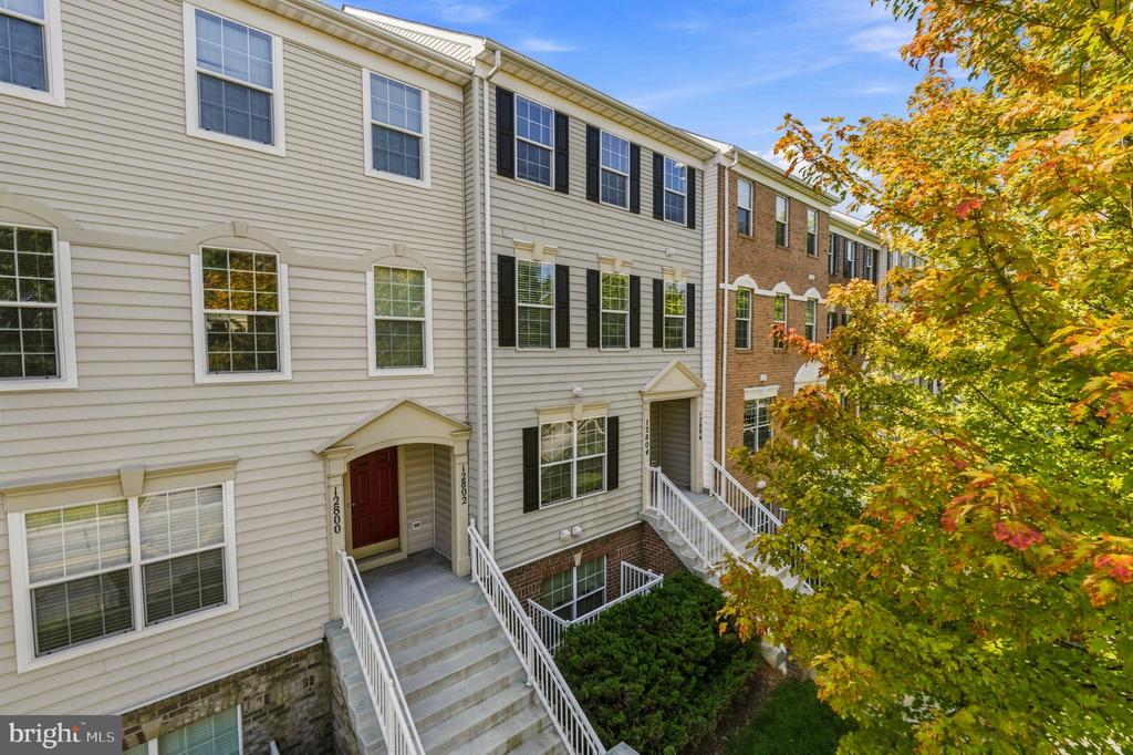 Attached townhomes with white stair railings and a red door, framed by autumn foliage.