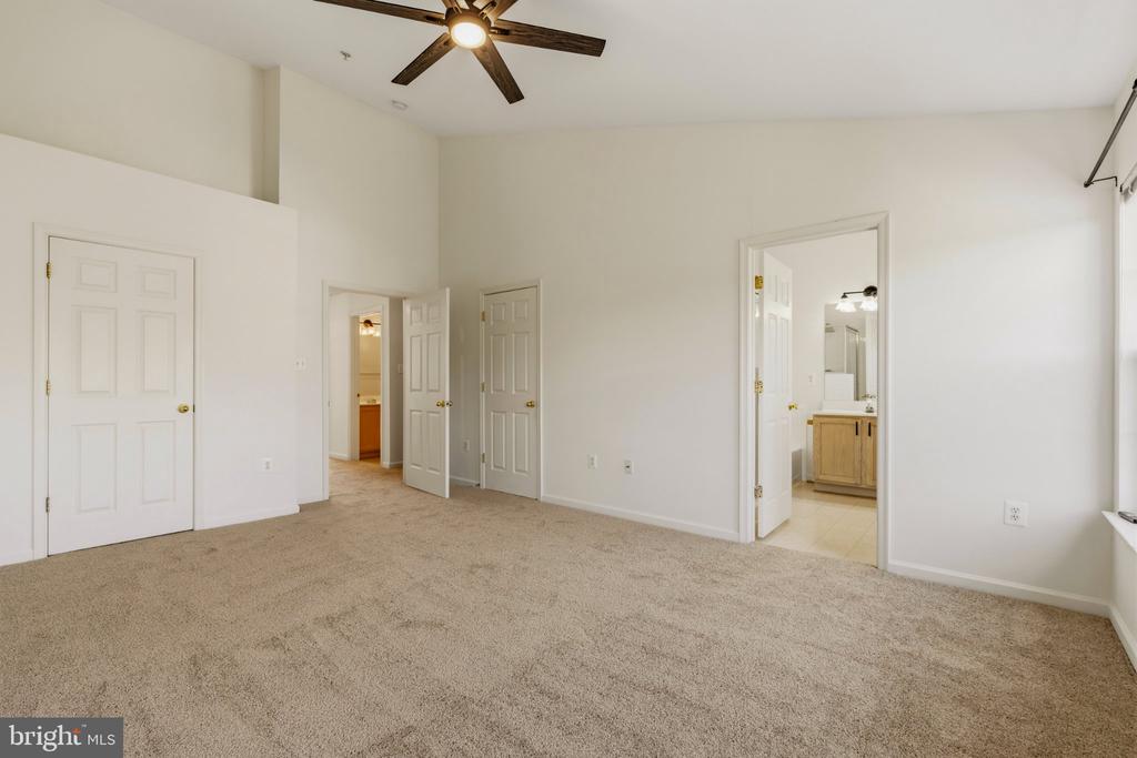 Empty carpeted bedroom with a ceiling fan and an open doorway to a bathroom.