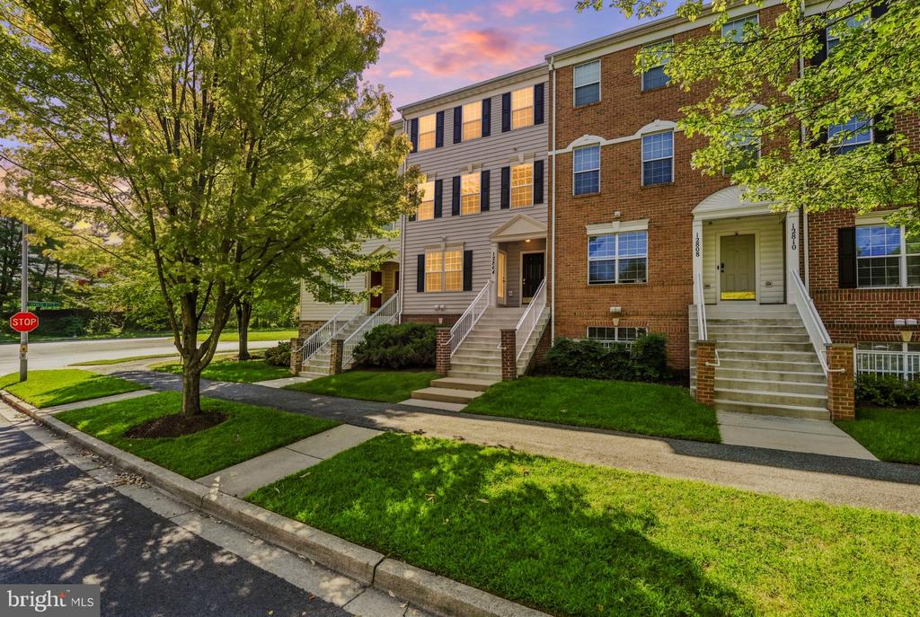 Attached townhomes with brick and gray siding, front steps, and mature trees along the sidewalk.