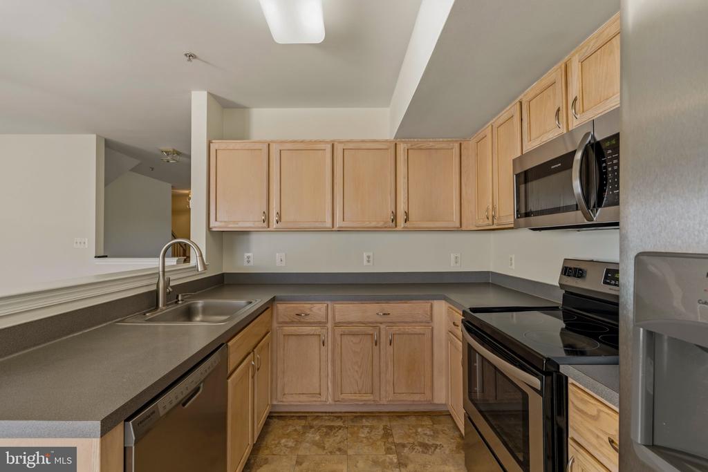 Kitchen with light wood cabinets, dark counters, and stainless-steel sink and dishwasher.