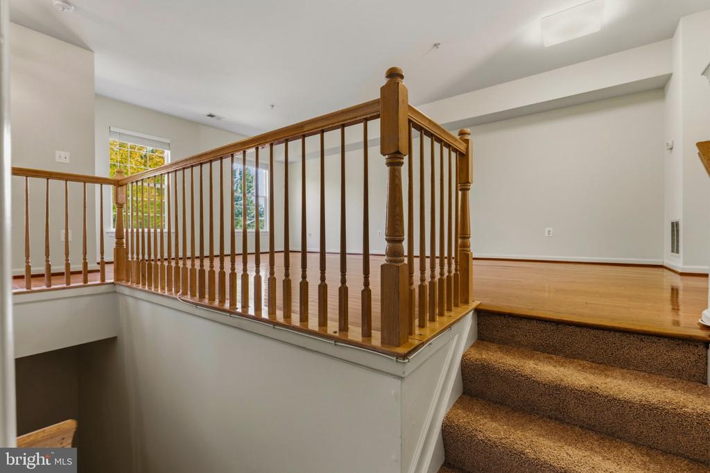 Open staircase with wooden railings, hardwood landing, and carpeted steps.