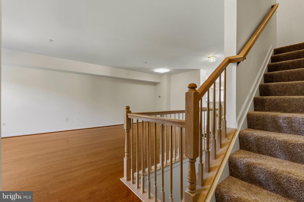Empty living area with hardwood floors beside a carpeted staircase and wooden railing.