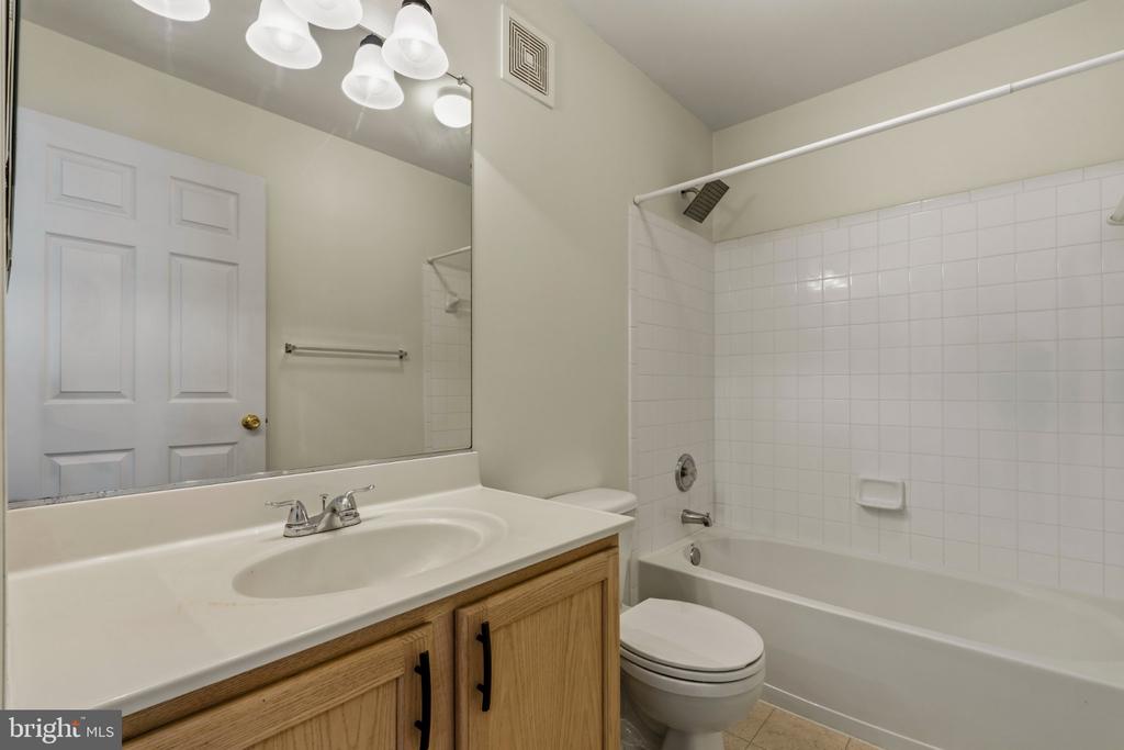 Bathroom with a white tub and tiled surround, toilet, and wood vanity beneath a large mirror.