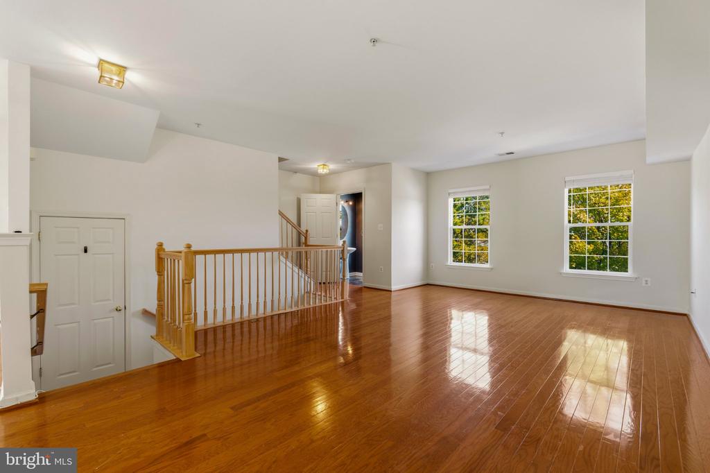 Empty upstairs living area with glossy hardwood floors, two windows, and a wooden stairwell railing.