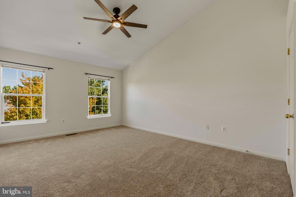 Vacant bedroom with beige carpet, a wood-blade ceiling fan, and two windows overlooking autumn foliage.