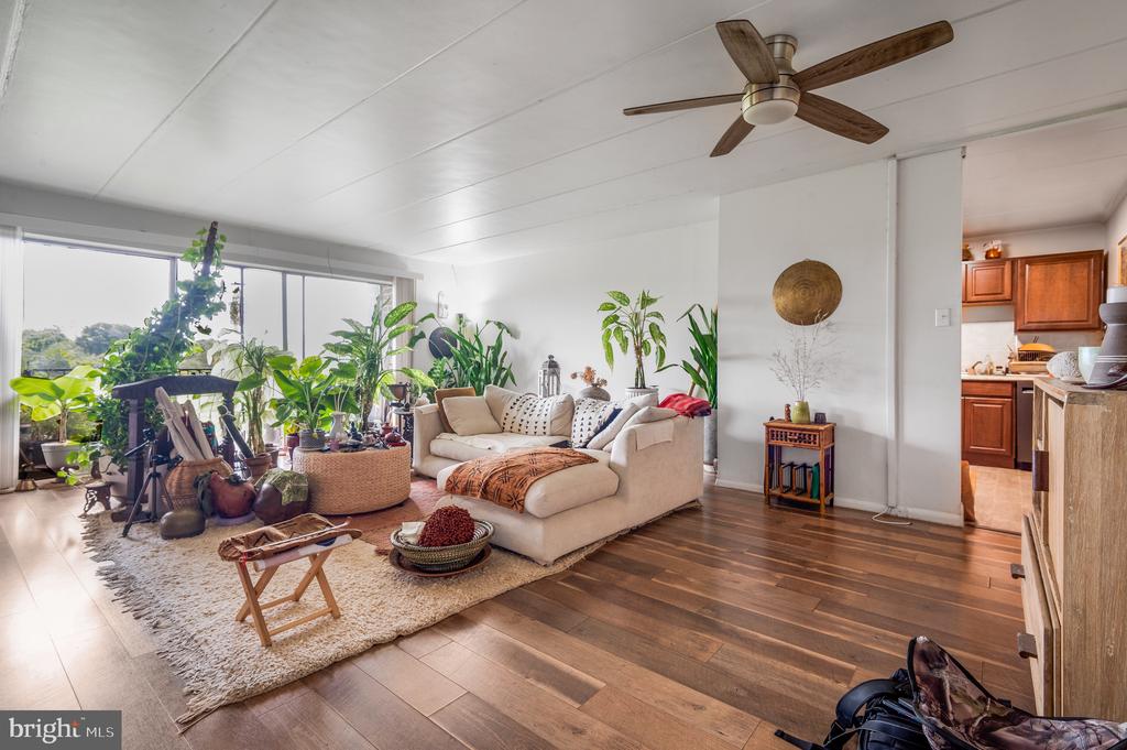 Furnished living room with a cream sectional, abundant houseplants, and wide windows.