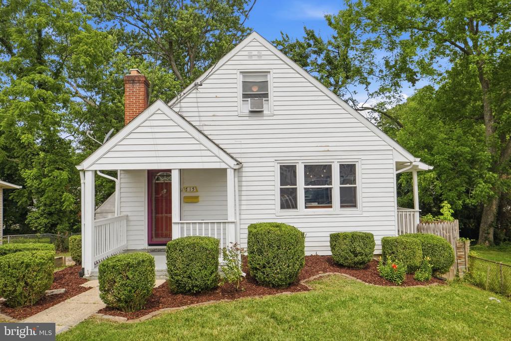 White gabled house with a red front door, covered porch, and landscaped shrubs.