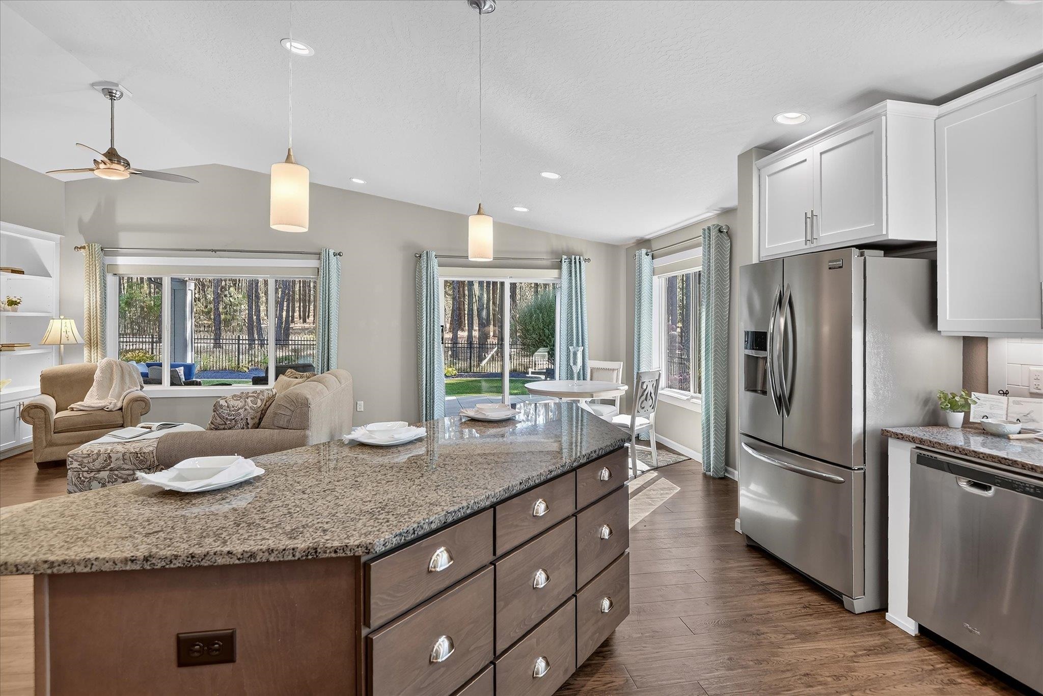 Open-plan kitchen with granite island and stainless appliances, adjoining a living area with backyard views.
