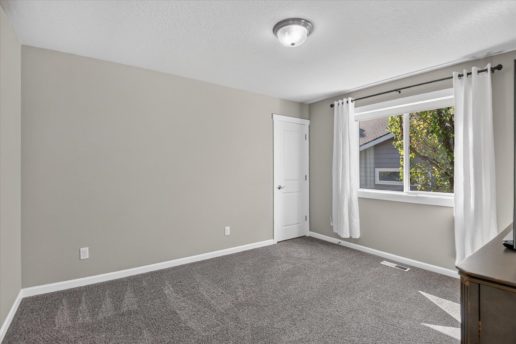 Empty bedroom with gray carpet and a large curtained window.