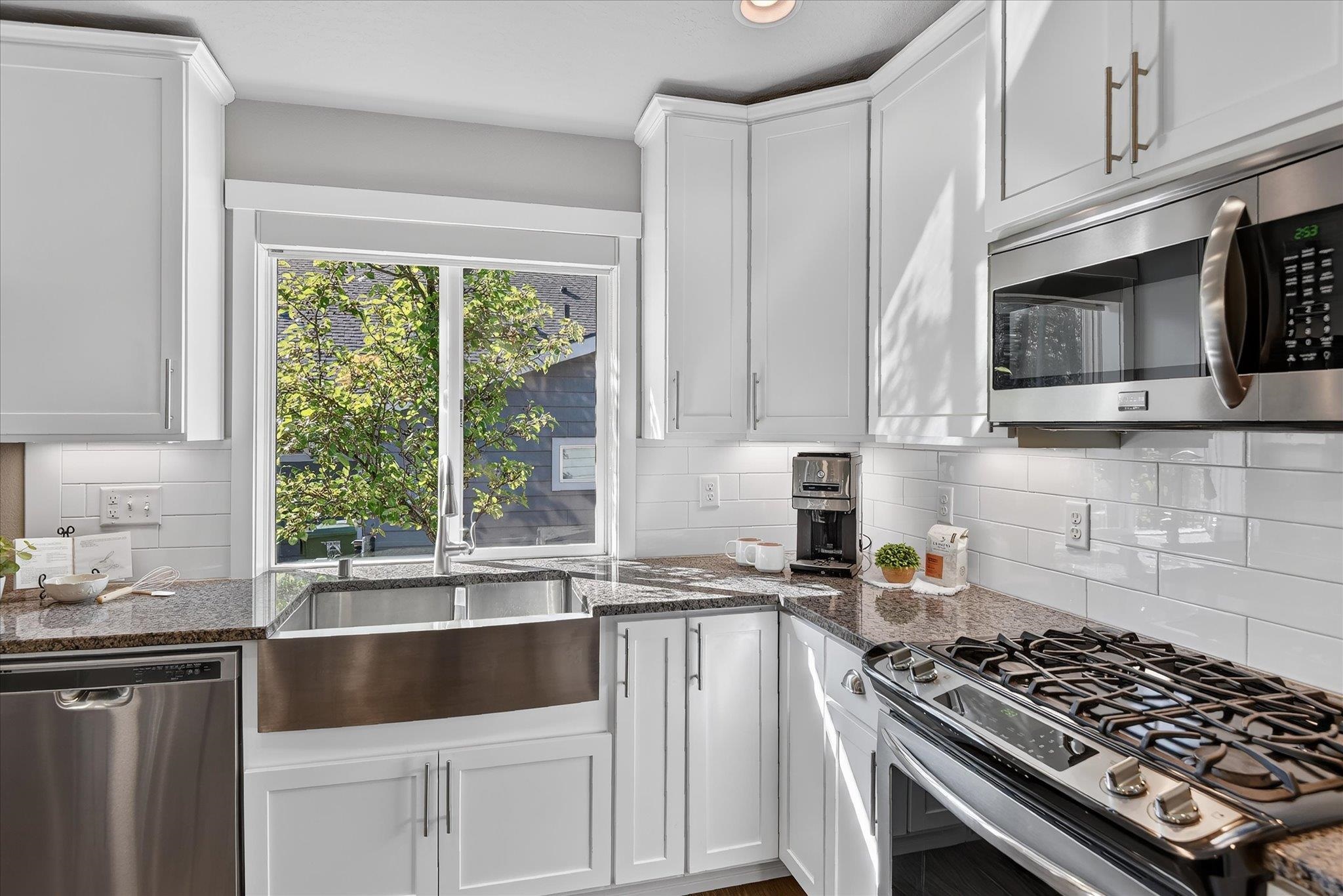 Bright white kitchen with a farmhouse sink beneath a window and stainless steel appliances.